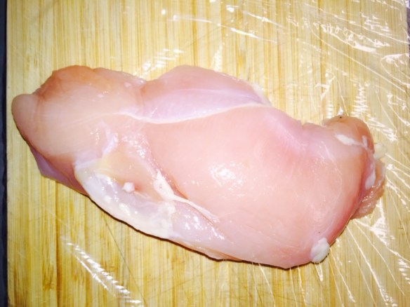 Lay breast on cutting board covered in plastic wrap